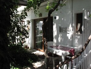 Un pequeño espacio al aire libre con mesa y sillas, rodeado por una valla blanca y follaje.