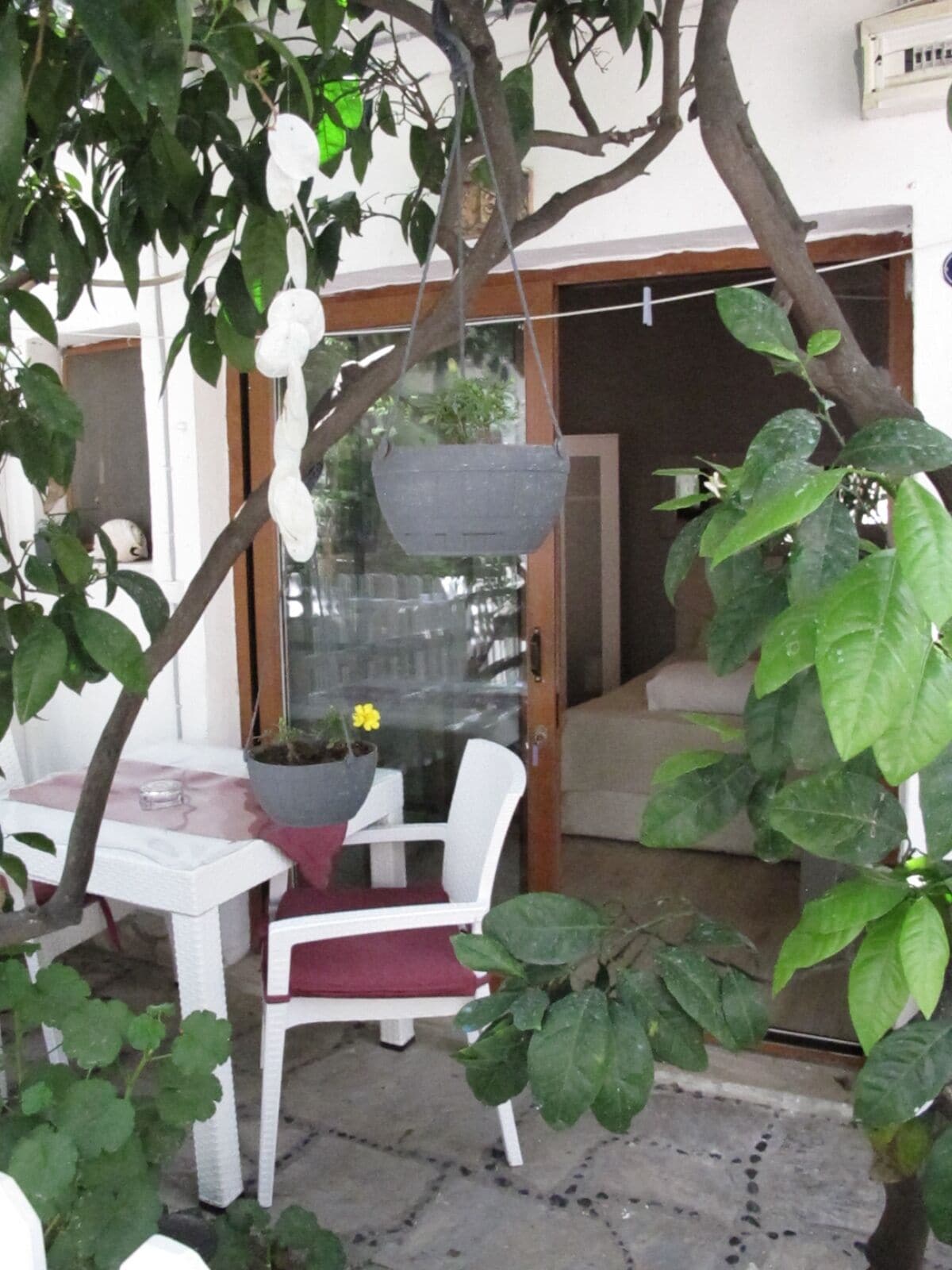 An outdoor seating area with a white table and chair, a hanging planter with a yellow flower, and a potted plant on the table.
