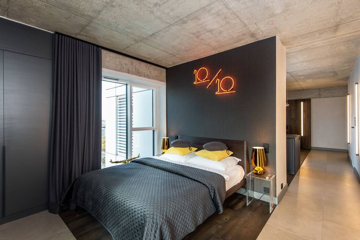 A modern bedroom with a large bed, a neon sign, and a view of the city.