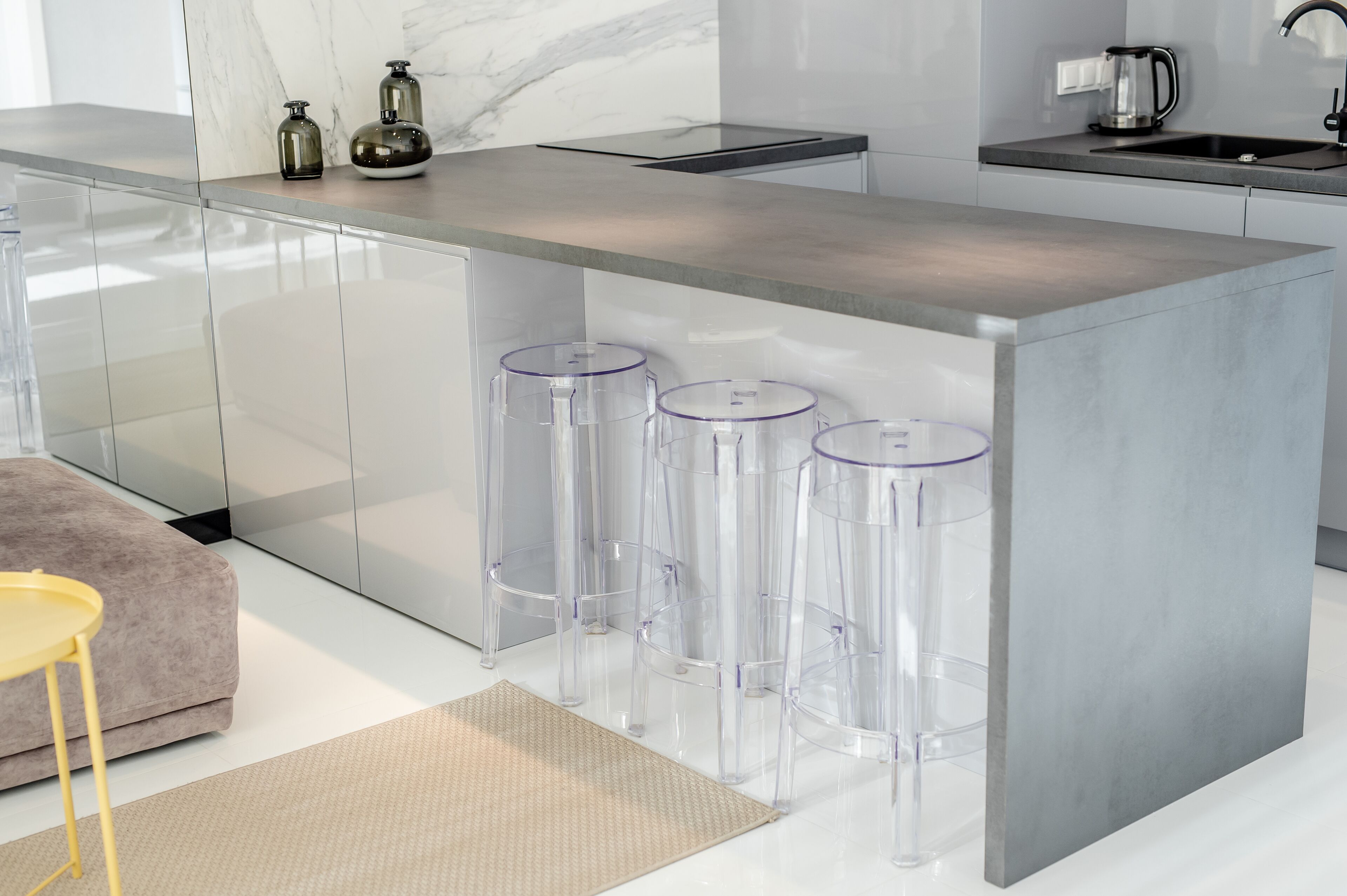 A modern kitchen with a marble countertop, a built-in island with bar stools, and a coffee maker.