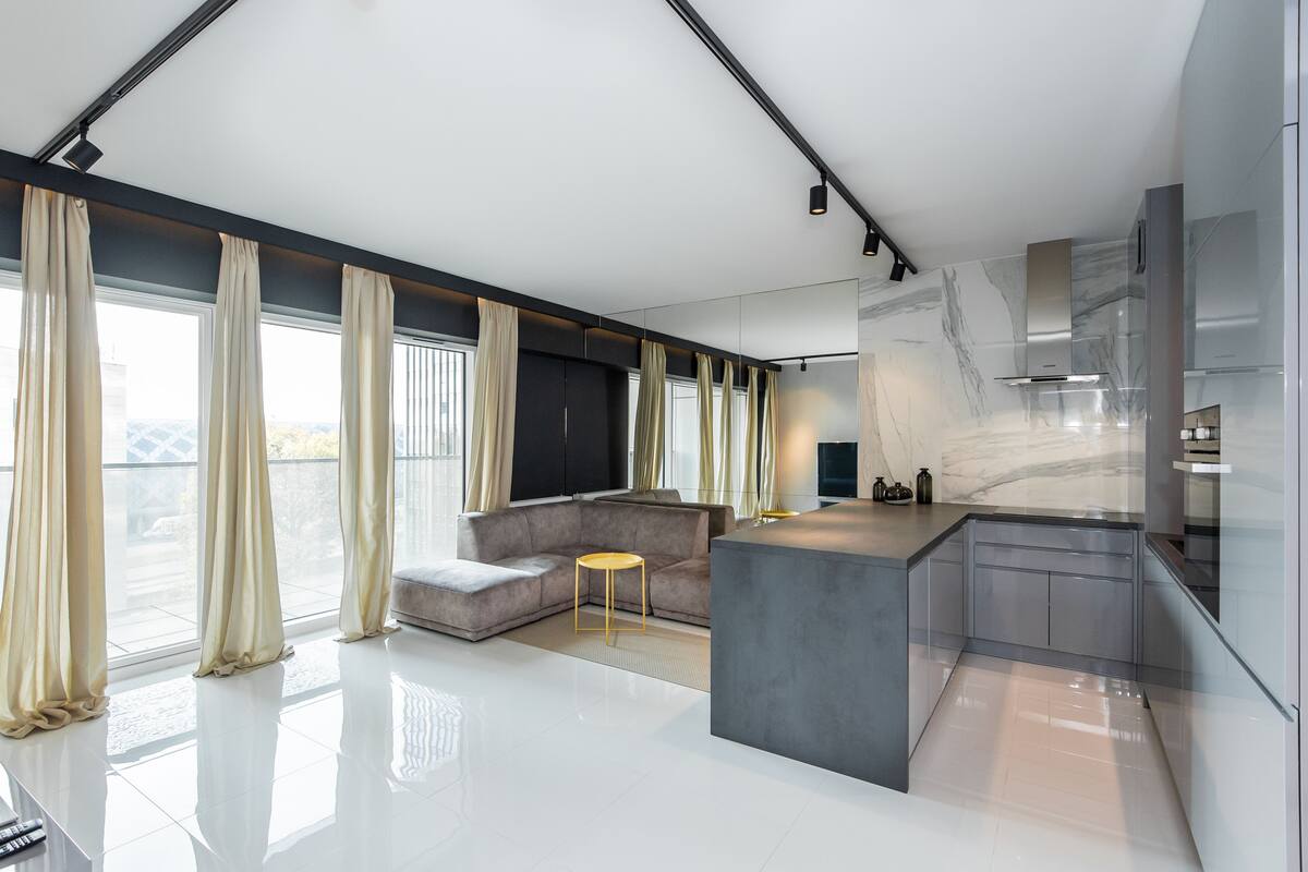 A modern living room with a grey sofa, a small round table, and a kitchen area with a marble backsplash.