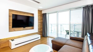 A modern living room with a flat-screen TV mounted on a wooden panel, a white entertainment unit, a glass coffee table, and a brown sofa. - SUPER-APARTAMENTY International Fair (Poznan)