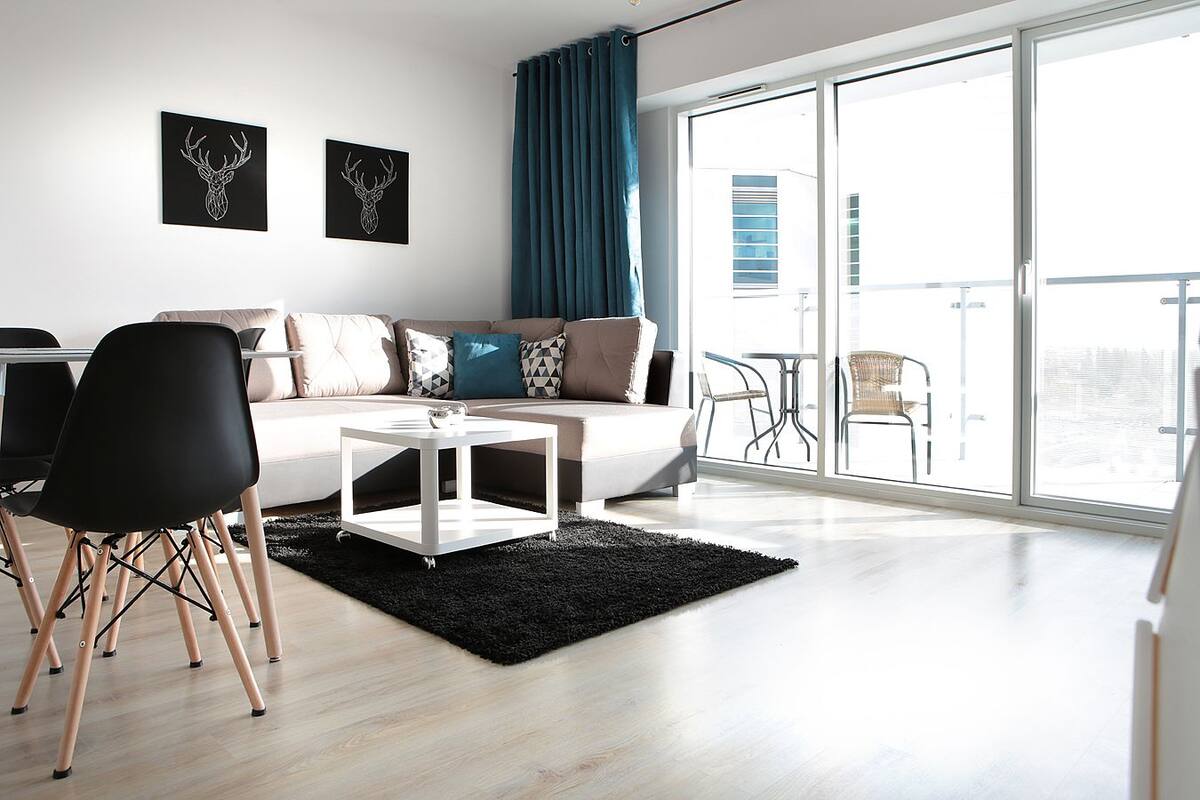 A modern living room with a sofa, a coffee table, and a dining area with chairs. There are two wall-mounted deer head art pieces.