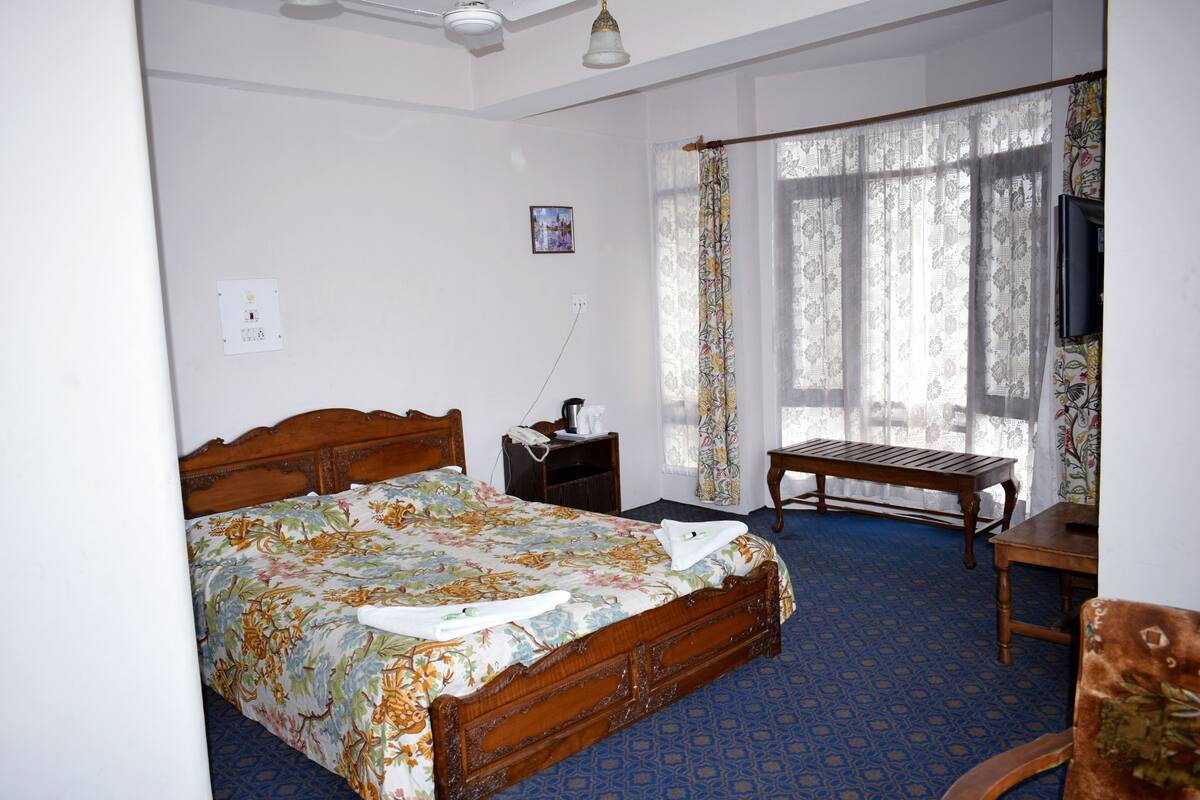 A bedroom with a wooden bed, a bedside table, a chair, and a window with curtains.