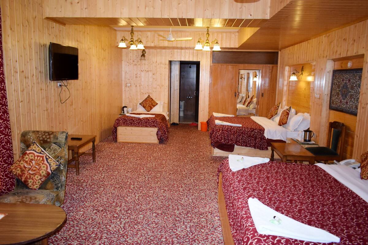 A hotel room with two beds, a television, a ceiling fan, and a wooden floor.