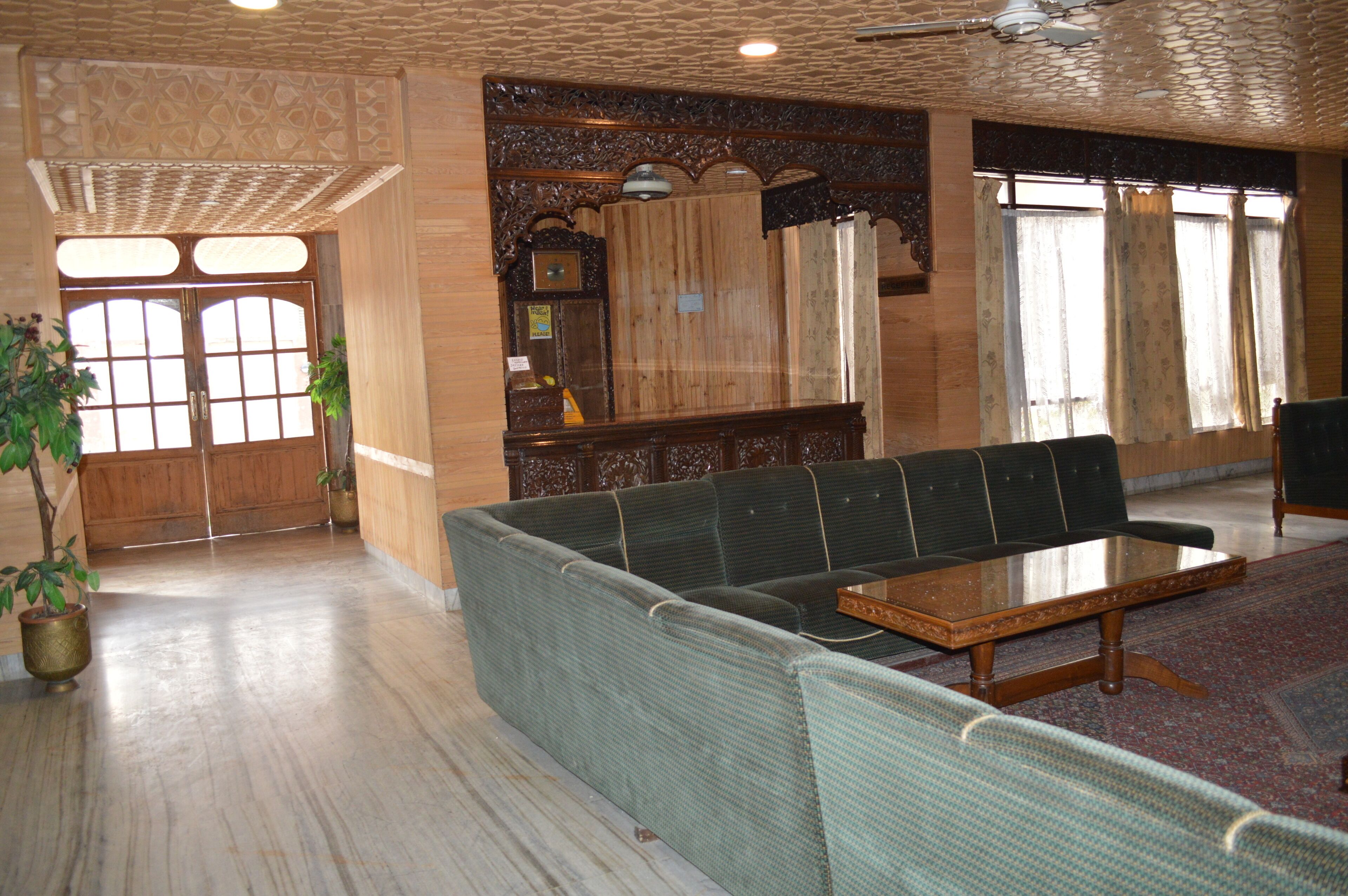 A spacious lobby with a green sofa, a wooden coffee table, and a large window with curtains.