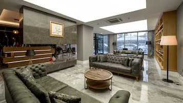 A spacious lobby with a marble floor, a reception desk, a sofa area, and a bookshelf.