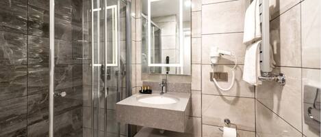 Un baño moderno con cabina de ducha de vidrio, tocador con espejo y perchero.