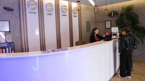 A reception desk with clocks indicating different cities, a counter with currency, and a plant in the background. - Sor Hotel Eskisehir (Eskisehir)