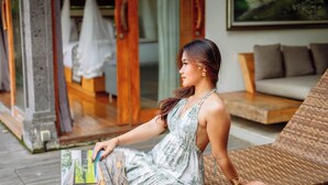 A woman sitting on a wicker chair in a room with a wooden floor and a sofa. - Ume Sri Villas Ubud (Ubud)