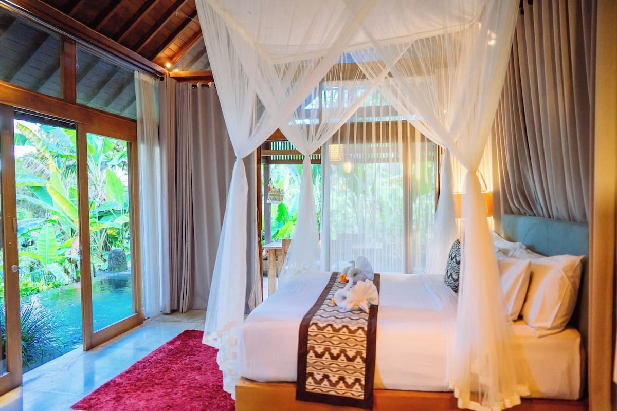A bedroom with a bed, a red rug, and a view of a garden and pool.