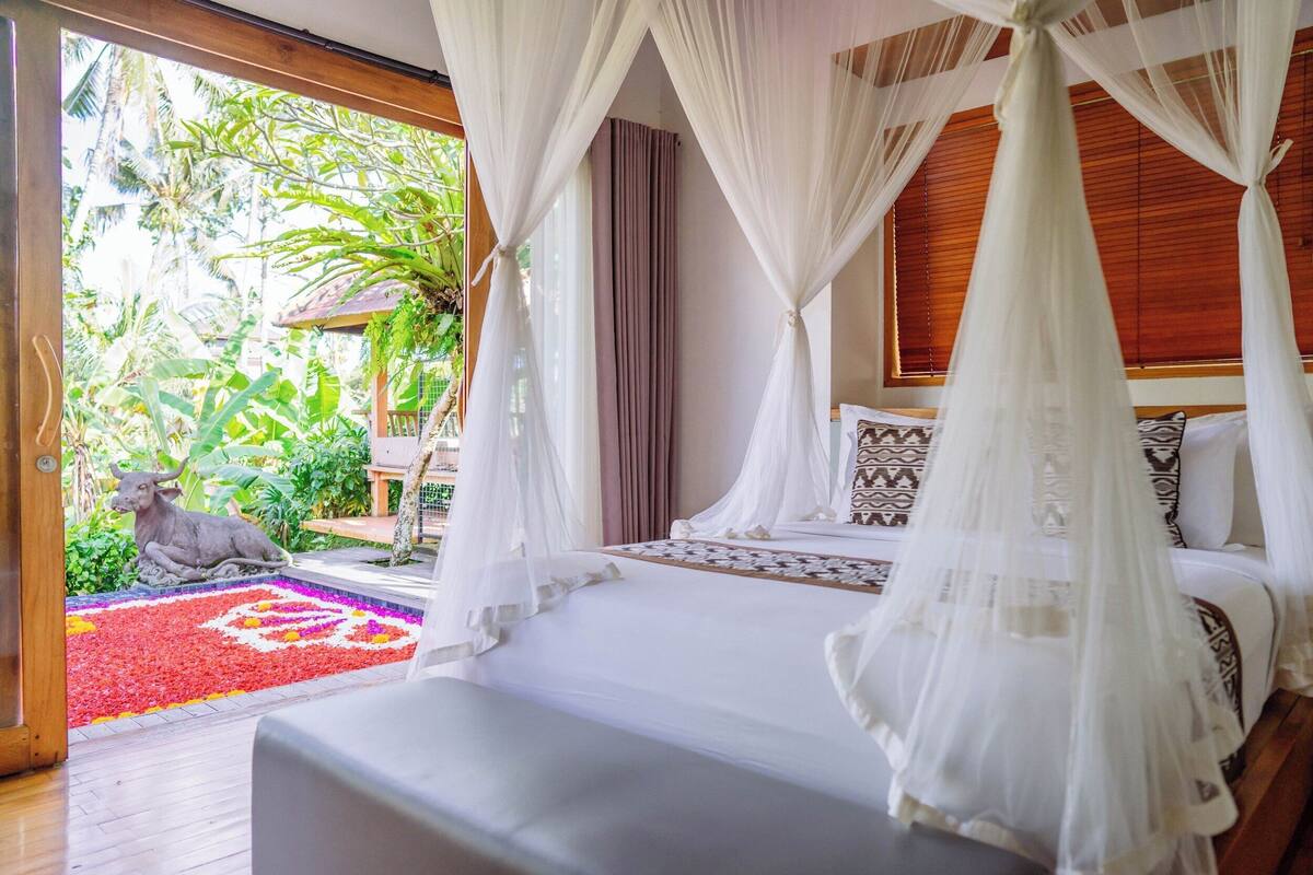 A bedroom with a canopy bed, a view of a garden, and a statue.