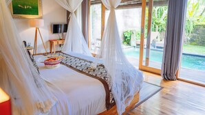 A bedroom with a bed, a bedside table, a lamp, a television, and a view of a swimming pool. - Ume Sri Villas Ubud (Ubud)