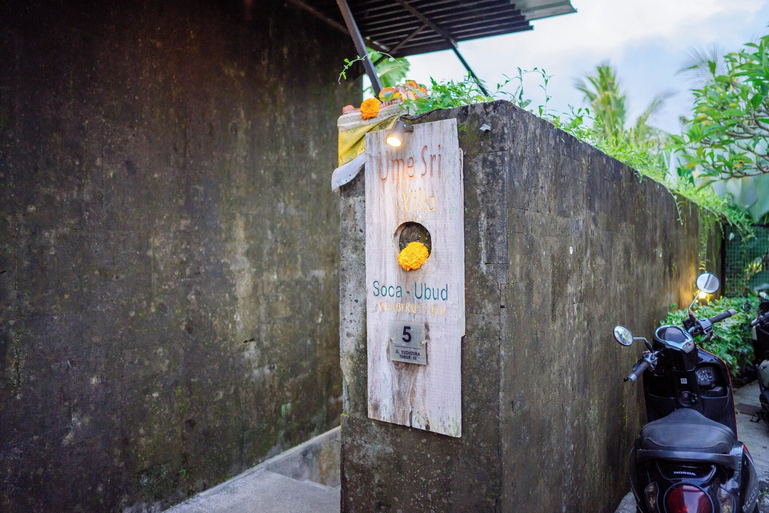 A concrete wall with a sign reading "Uma Sri Villa" and "Soca-Ubud" with a number "5" below.