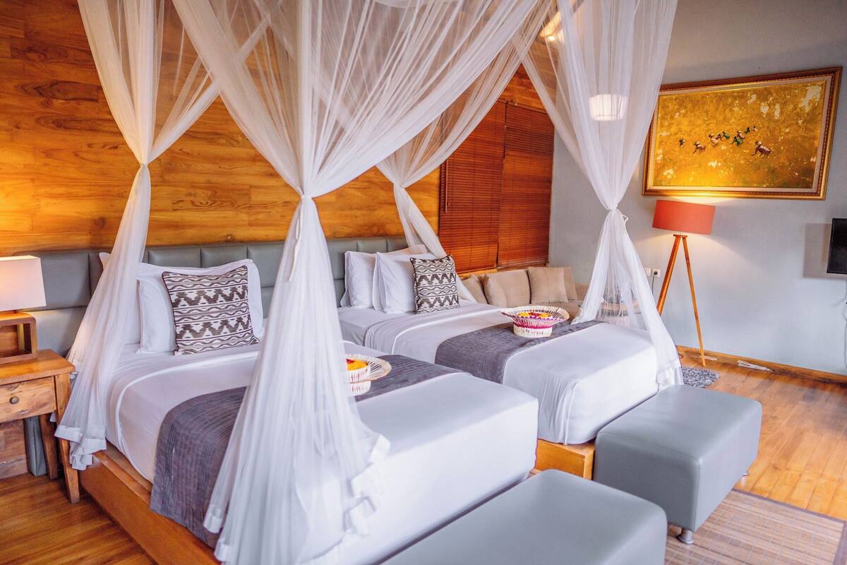 A bedroom with two beds, each with a canopy, a bedside table, a lamp, and a wall-mounted TV.