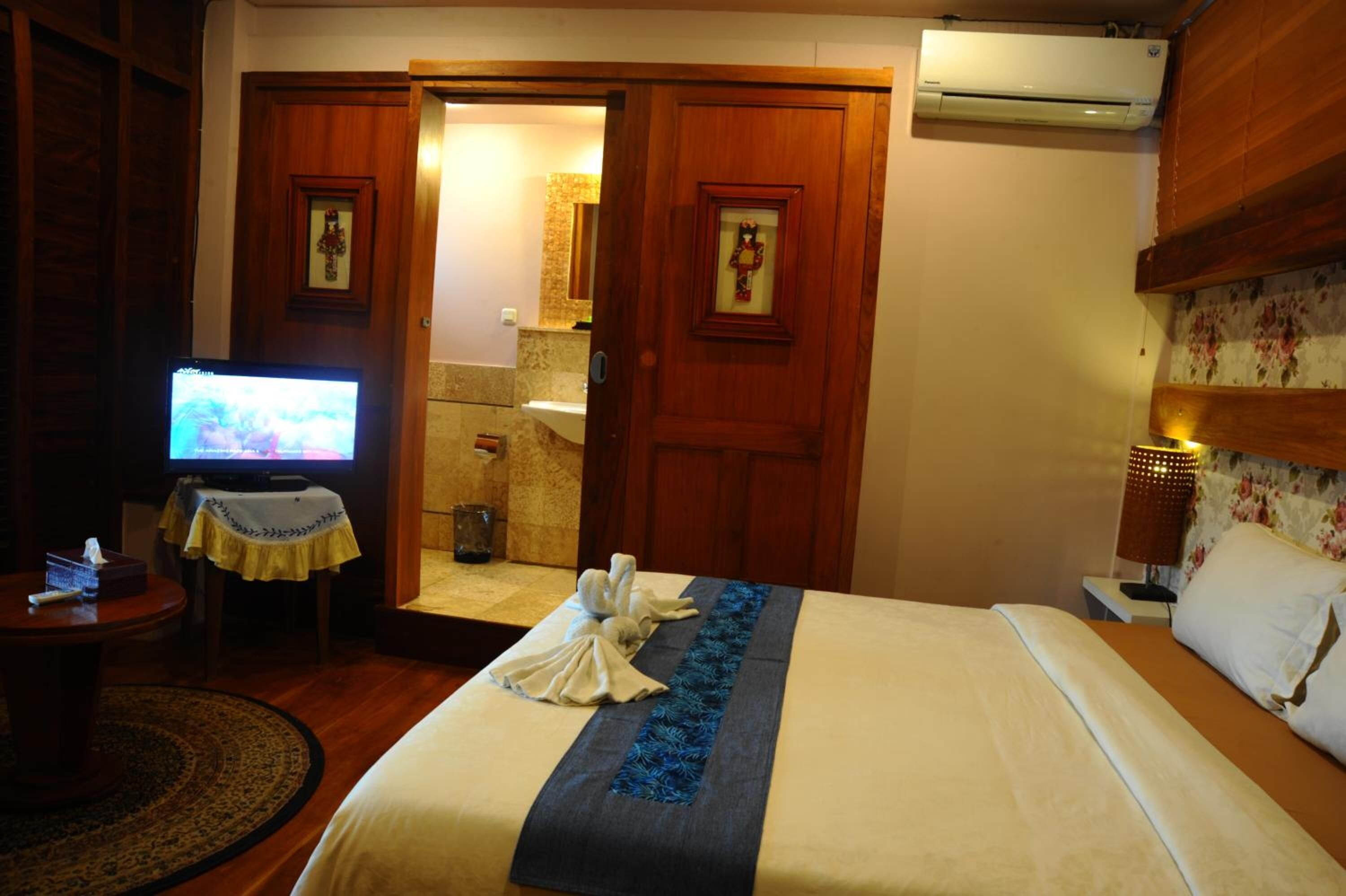 Habitación de hotel con cama, televisión, baño visible a través de una puerta abierta y un armario de madera.