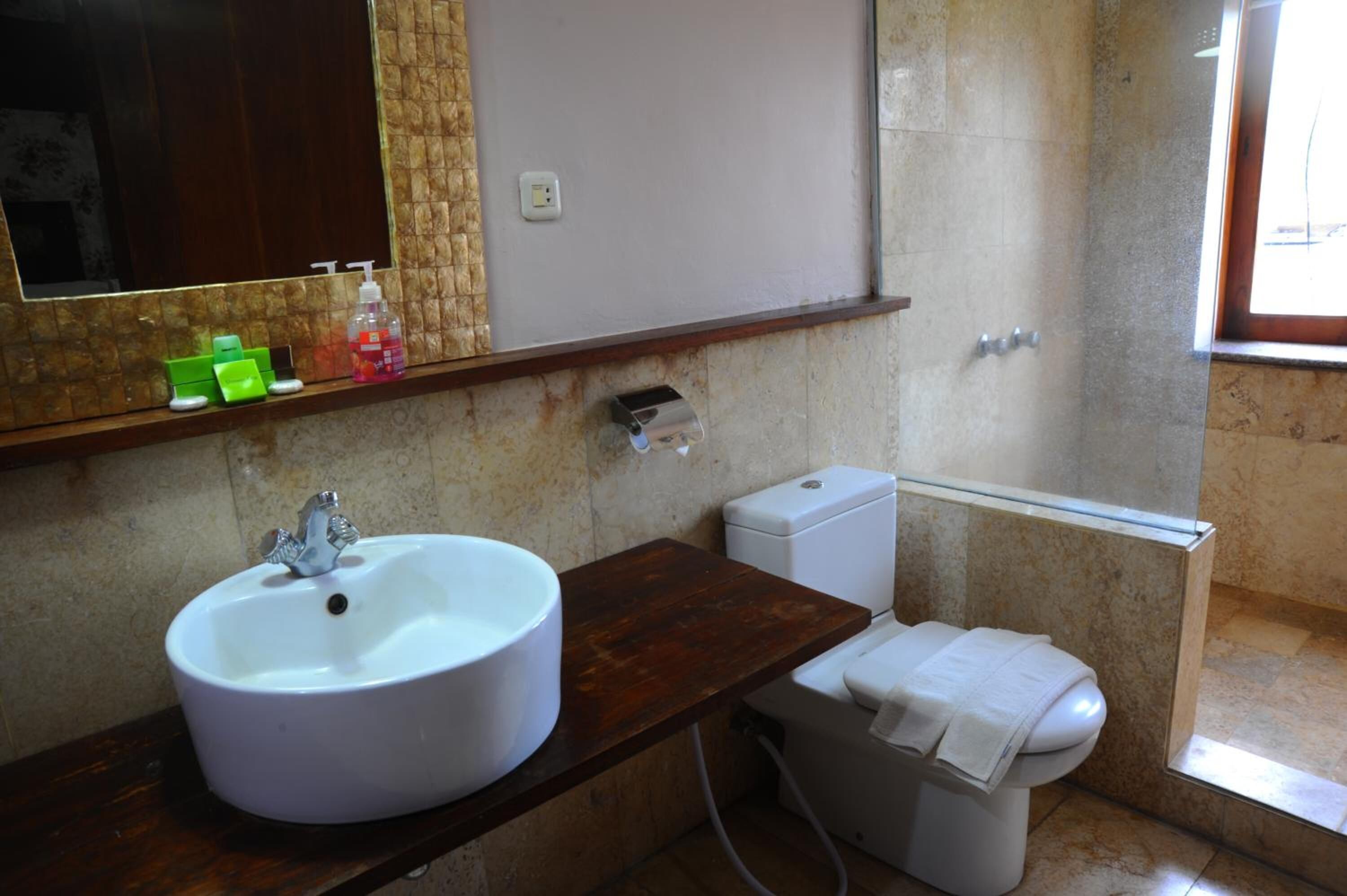 A bathroom with a white sink, a toilet, and a mirror. There are toiletries on the sink and a towel on the toilet.