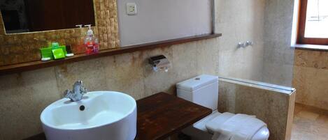 A bathroom with a white sink, a toilet, and a mirror. There are toiletries on the sink and a towel on the toilet.