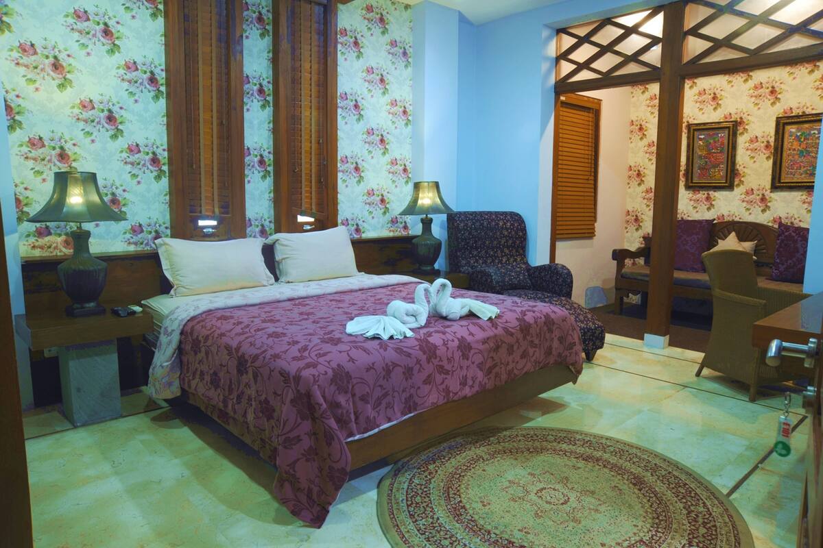 A bedroom with a bed, two nightstands, a chair, a desk, and a small table.