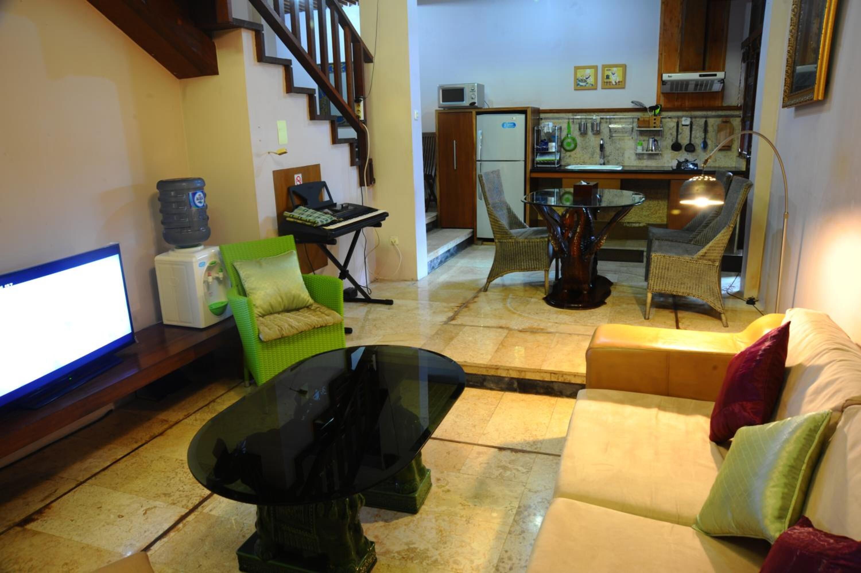 A living room with a sofa, a glass coffee table, a television, a water dispenser, and a kitchen area with a microwave, chairs, and a dining table.