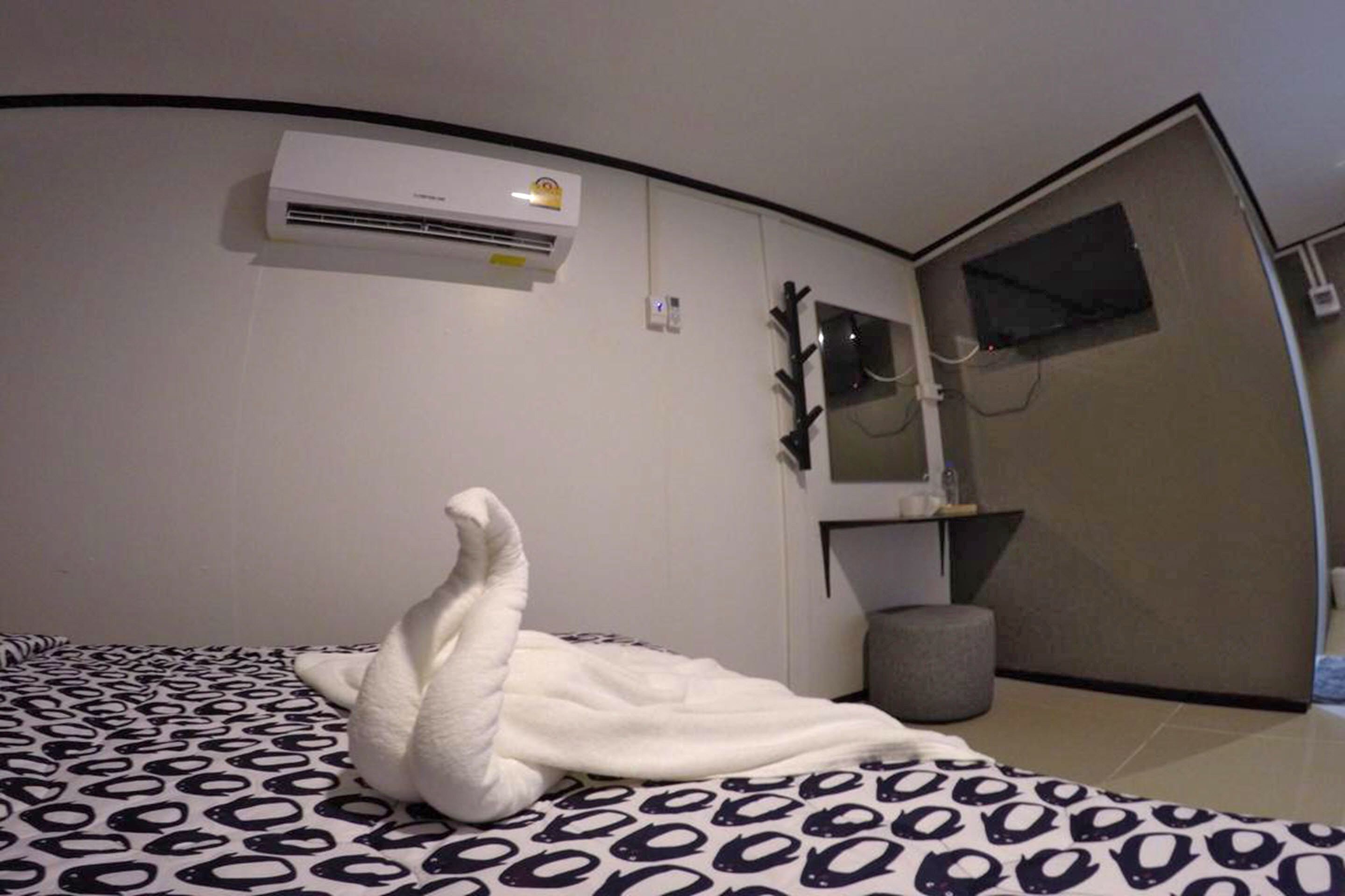 Una camera da letto moderna con un letto, un condizionatore d'aria a parete, uno specchio e uno sgabello.