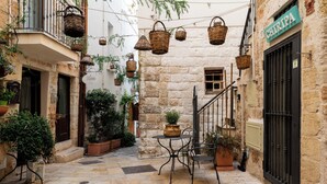 A narrow stone-paved alley with a small outdoor seating area, wicker baskets hanging overhead, and potted plants. - Santo Stefano Home & Breakfast (Polignano a Mare)