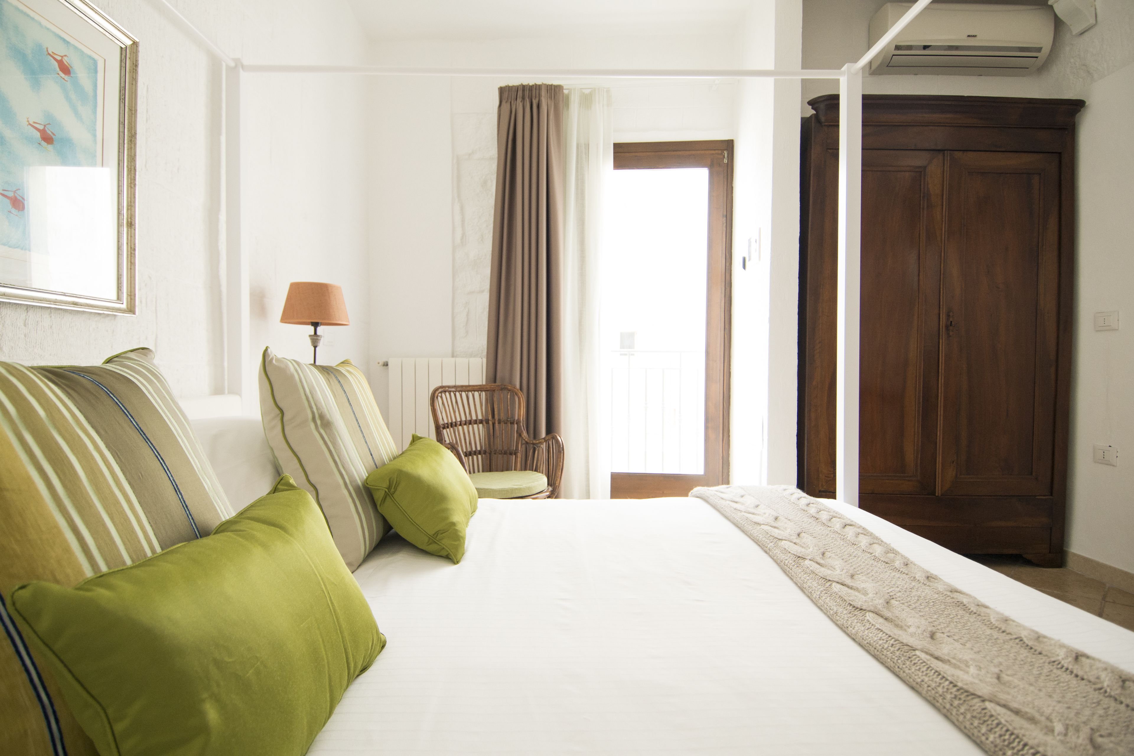 Ein Hotelzimmer mit einem großen Bett, grünen Kissen, einem Holzschrank und einem Sessel.