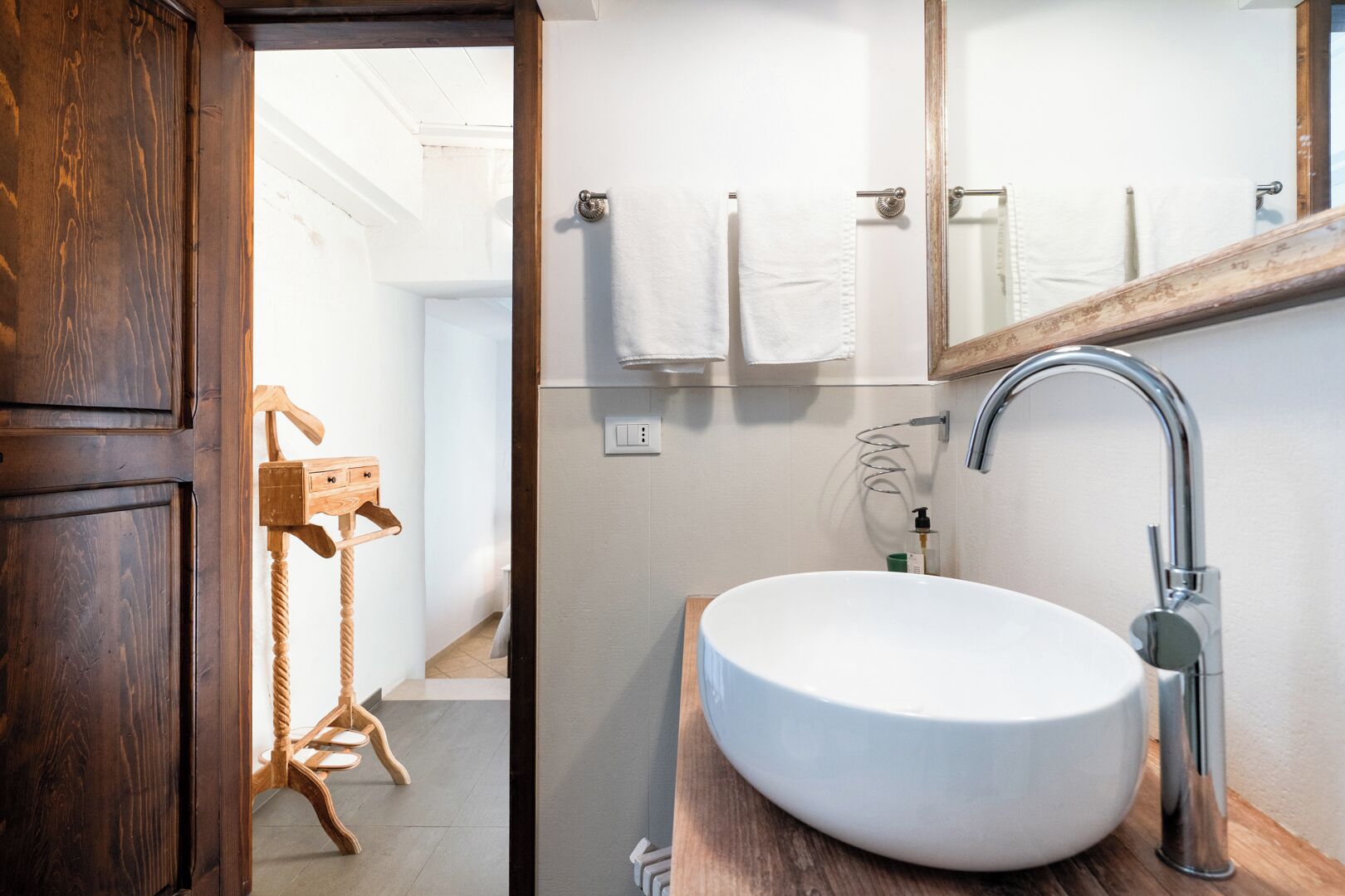 A bathroom with a wooden door, a white sink, a mirror, and a towel rack.