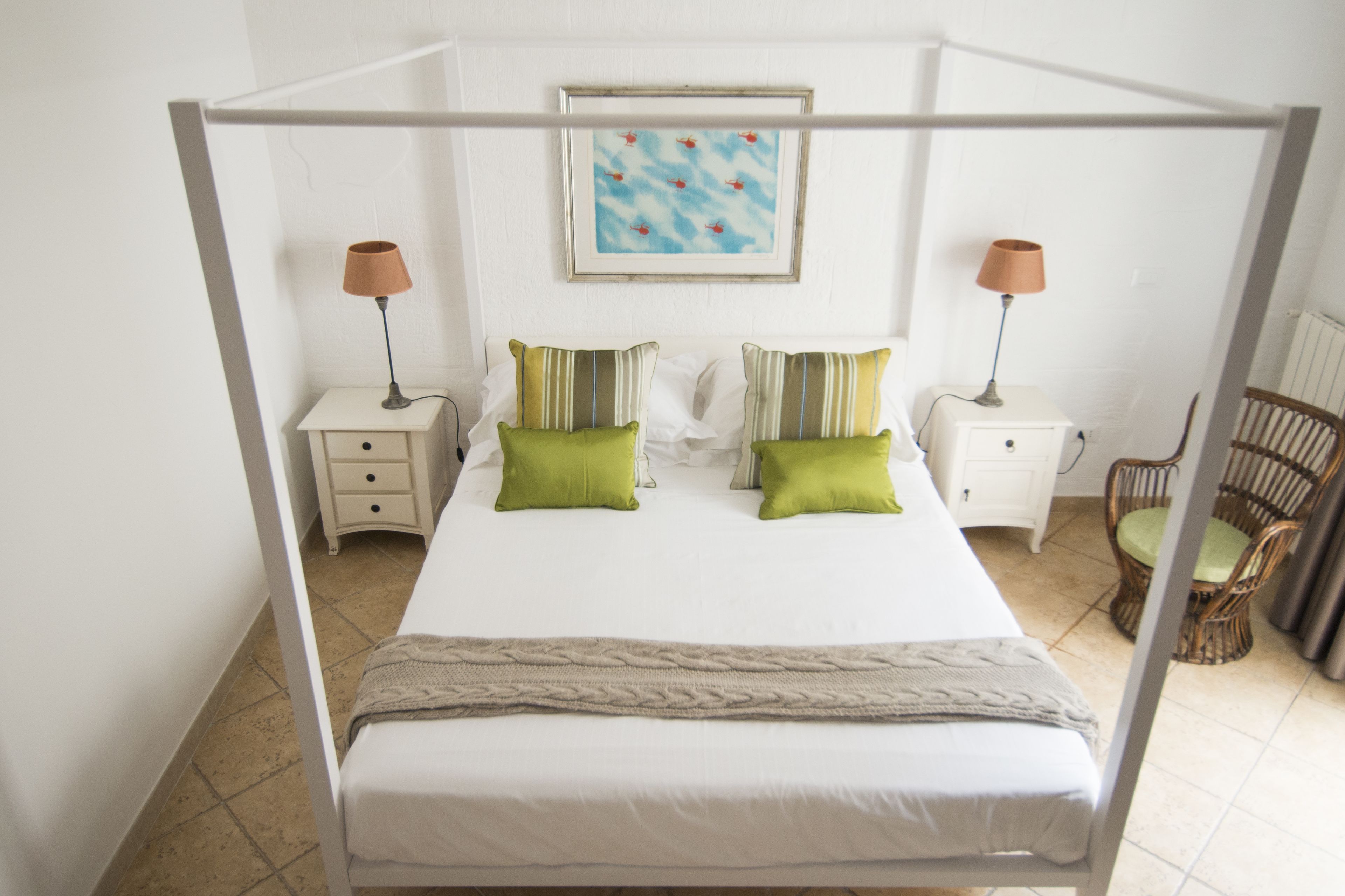 A four-poster bed with two nightstands, each with a lamp, and a wicker chair.