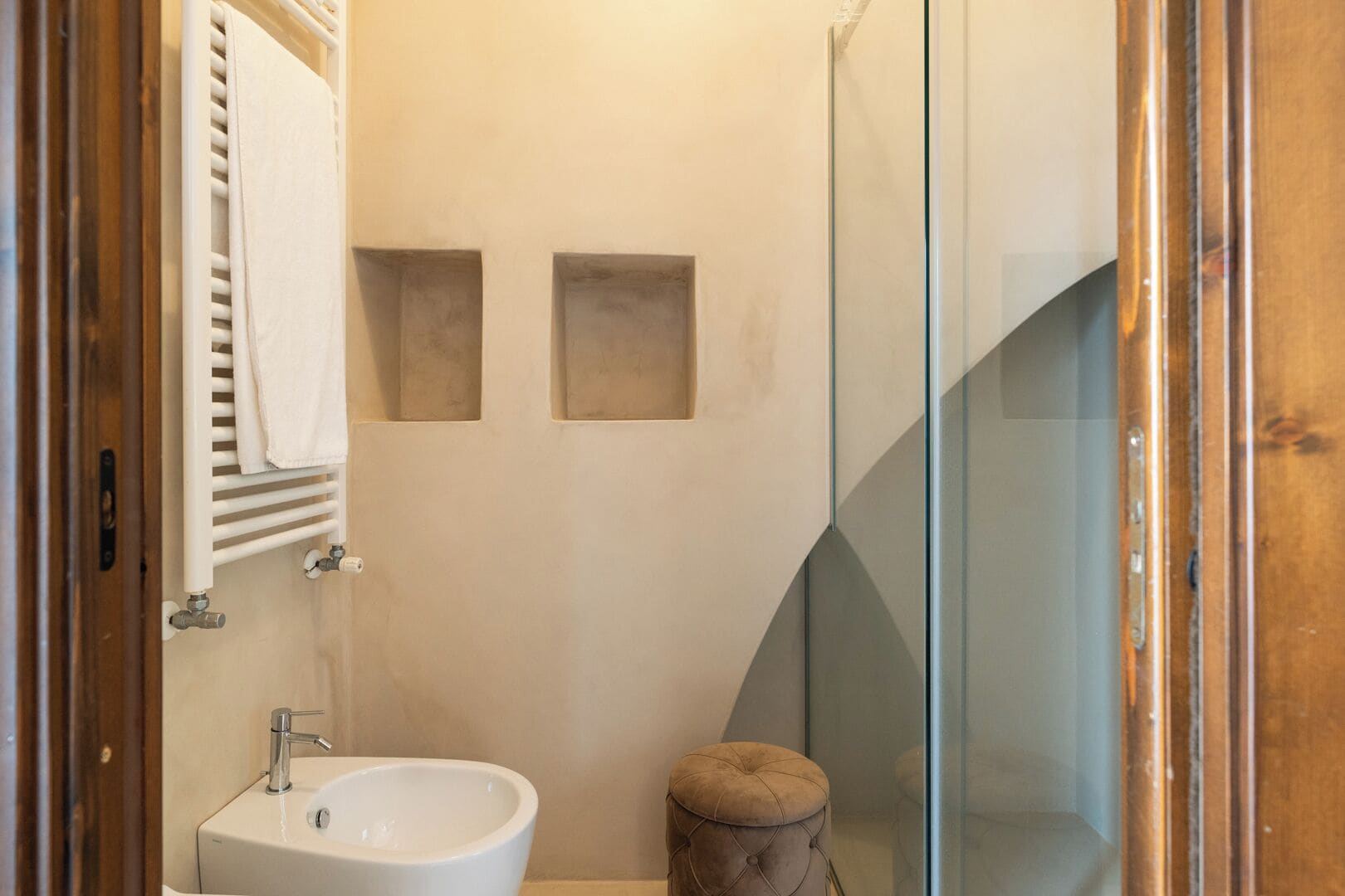 A bathroom with a white sink, a mirror, and a towel rack. There are two square mirrors on the wall and a glass shower enclosure.