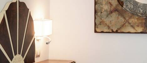 A neatly made bed with white linens, a wooden nightstand with a lamp, and a wall-mounted mirror with a decorative frame.