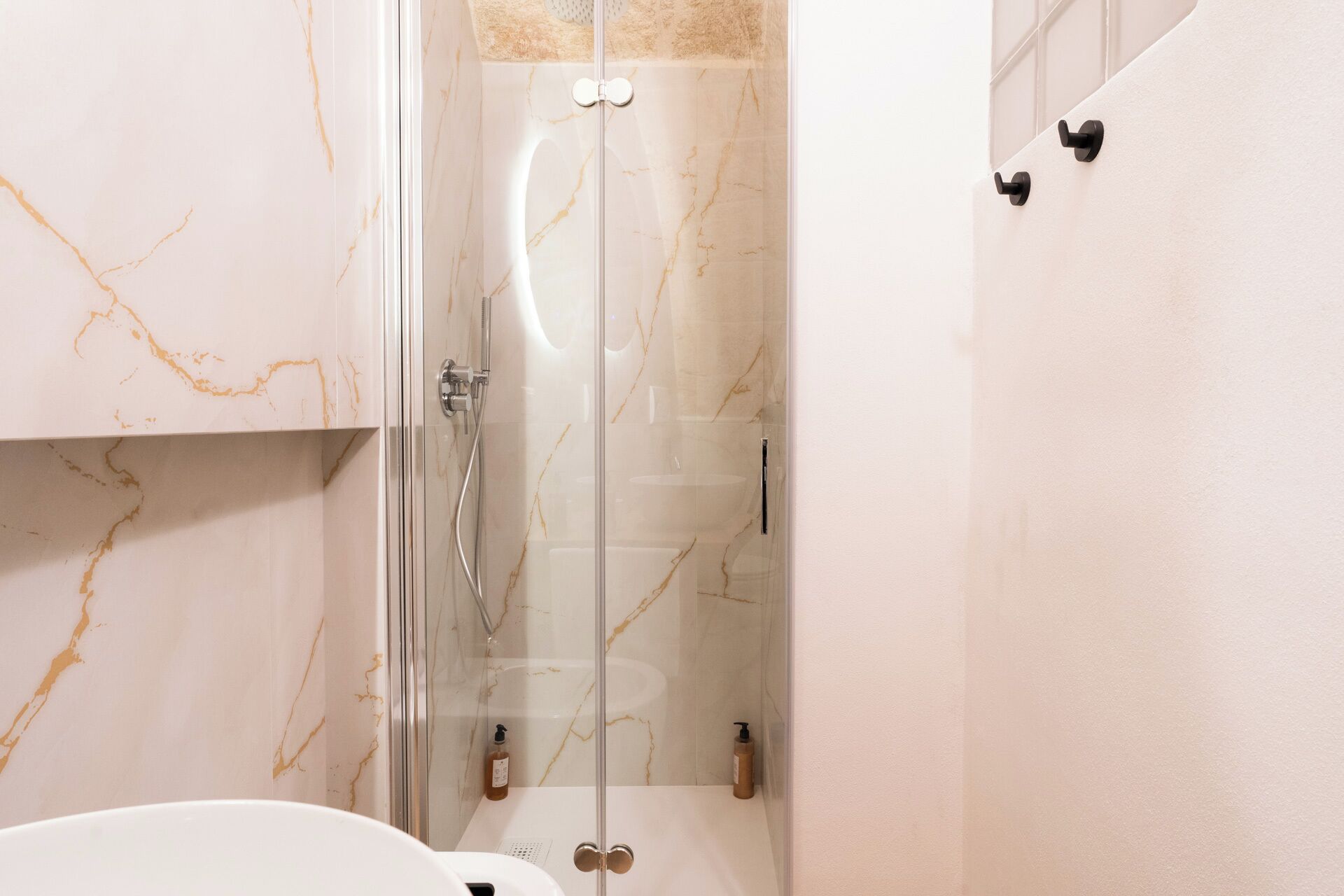 A modern bathroom with a glass-enclosed shower, marble walls, and a white sink.