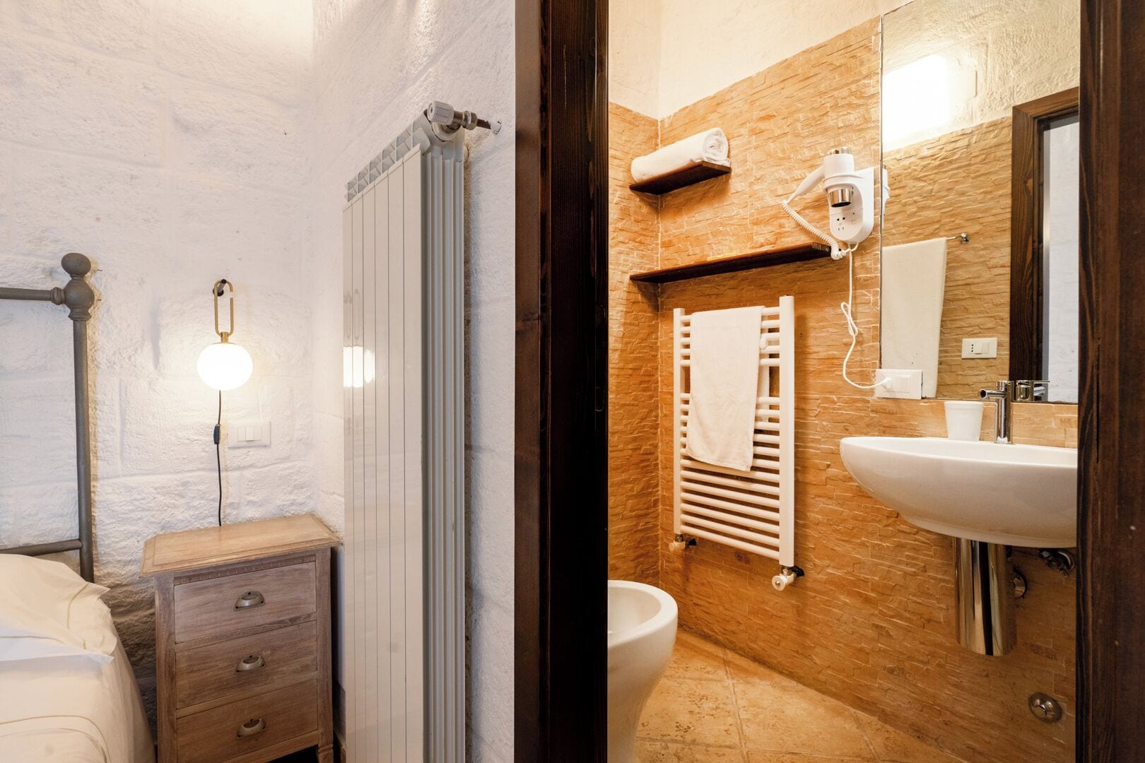 Un baño con suelo de madera, un radiador blanco, un perchero para toallas, un lavabo y un espejo.