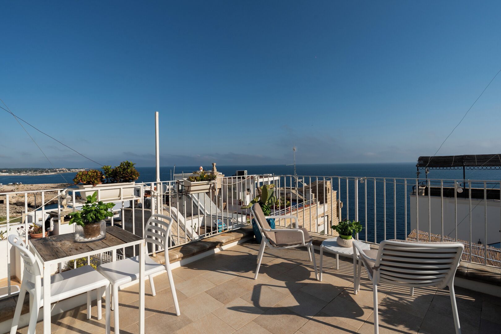 A terrace with white furniture, potted plants, and a view of the sea.