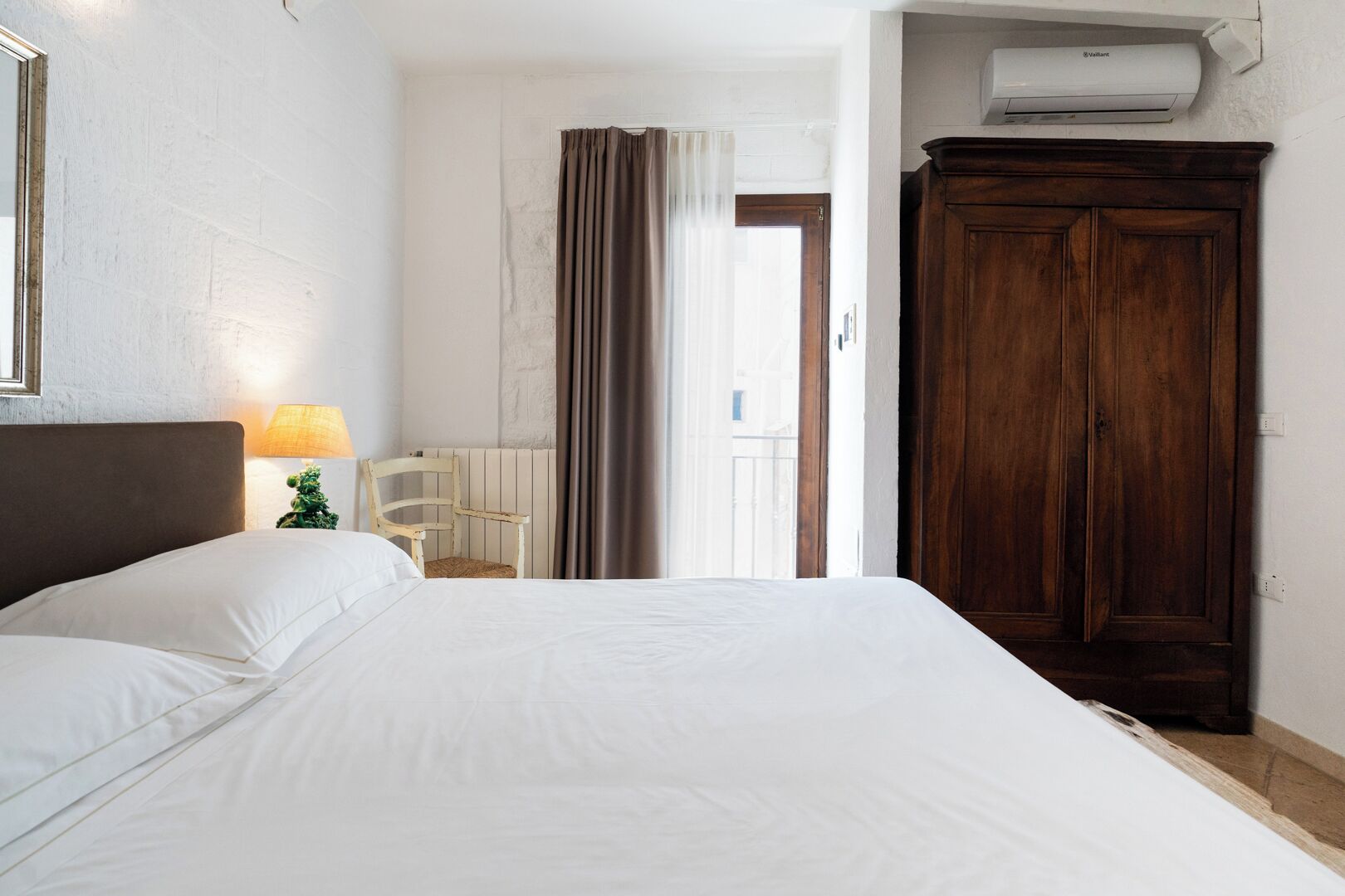 A bedroom with a large bed, a wooden wardrobe, a chair, a lamp, and a radiator.