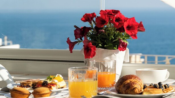 A table with breakfast items, a vase of red flowers, and a view of the sea. - Santo Stefano Home & Breakfast (Polignano a Mare)