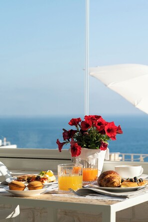 Une table avec des aliments pour le petit-déjeuner, un vase rempli de fleurs rouges et une vue sur la mer.