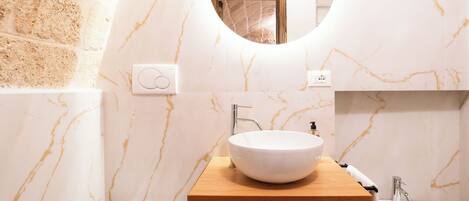 A bathroom with a round mirror, a wooden vanity, a white sink, a bathtub, and a shower.