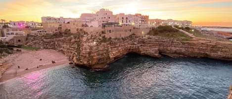 Un pueblo costero con una imponente formación rocosa y un puente que lo conecta a tierra firme.