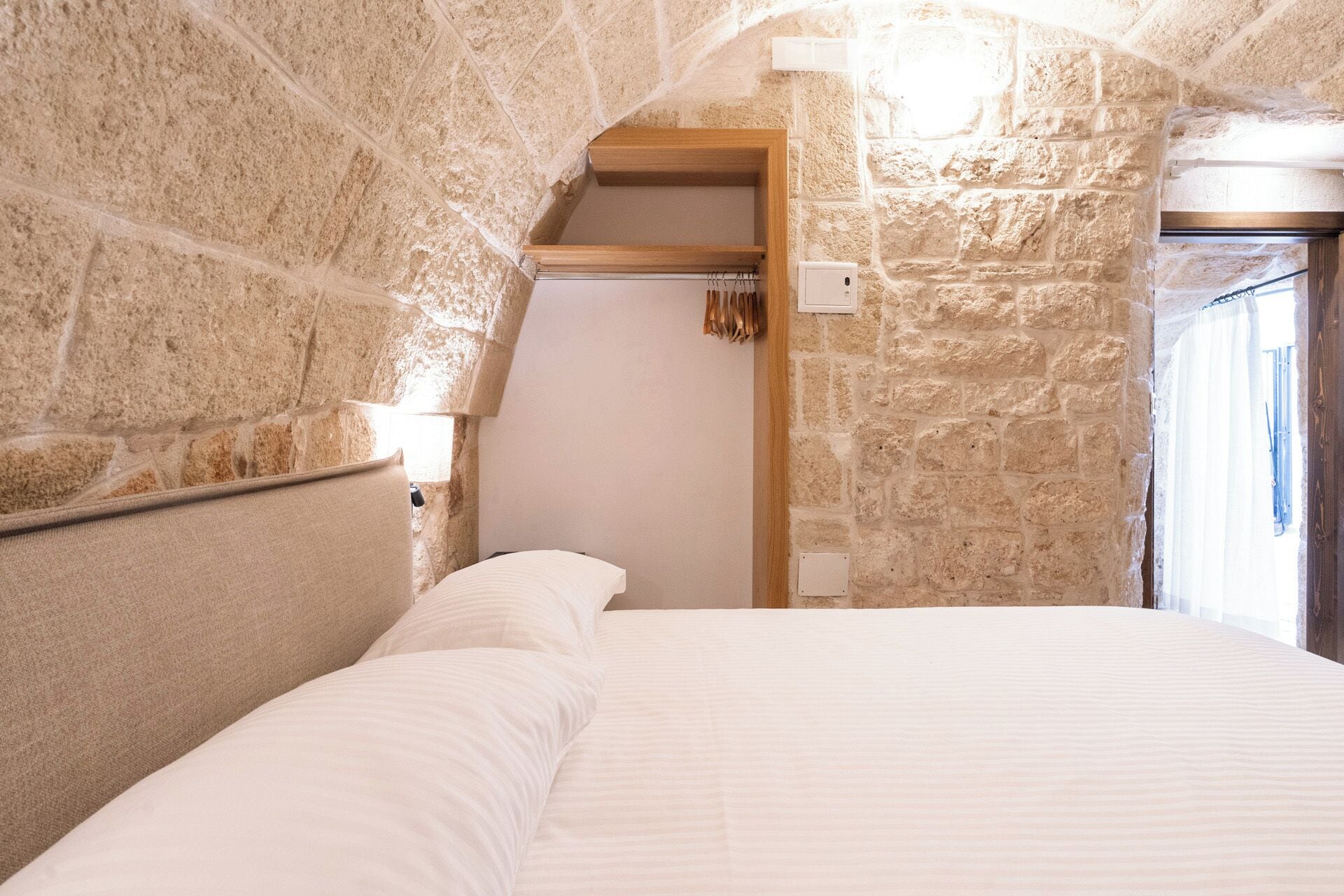A bedroom with stone walls, a wooden headboard, and a white bed.
