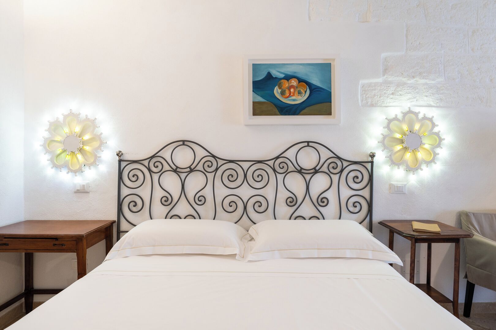 A neatly made bed with a decorative headboard, two bedside tables with lamps, and a painting on the wall.