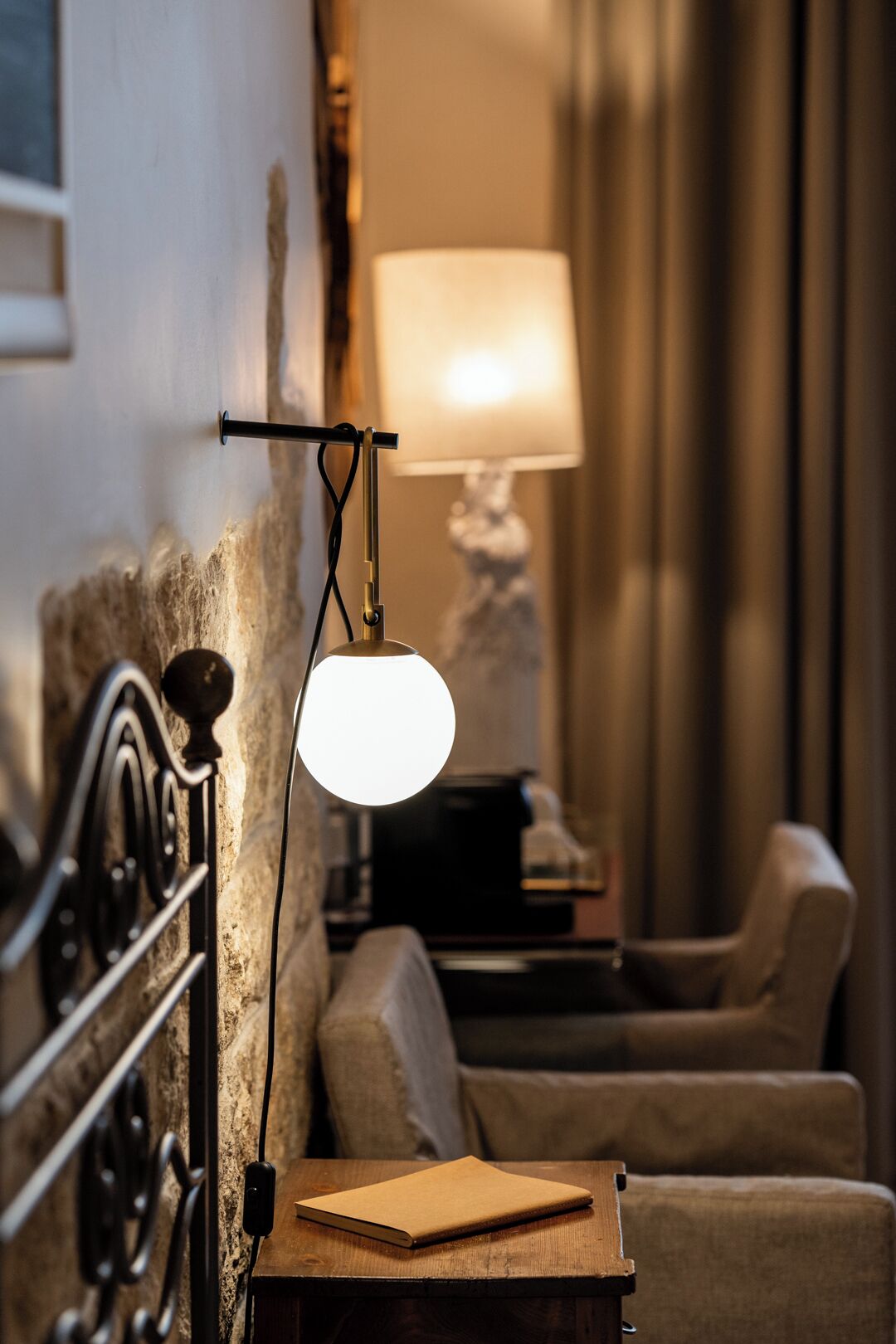 Ein gemütliches Zimmer mit einem Holfnachtkästchen, einer Lampe, einer Couch und einer dekorativen Lampe im Hintergrund.