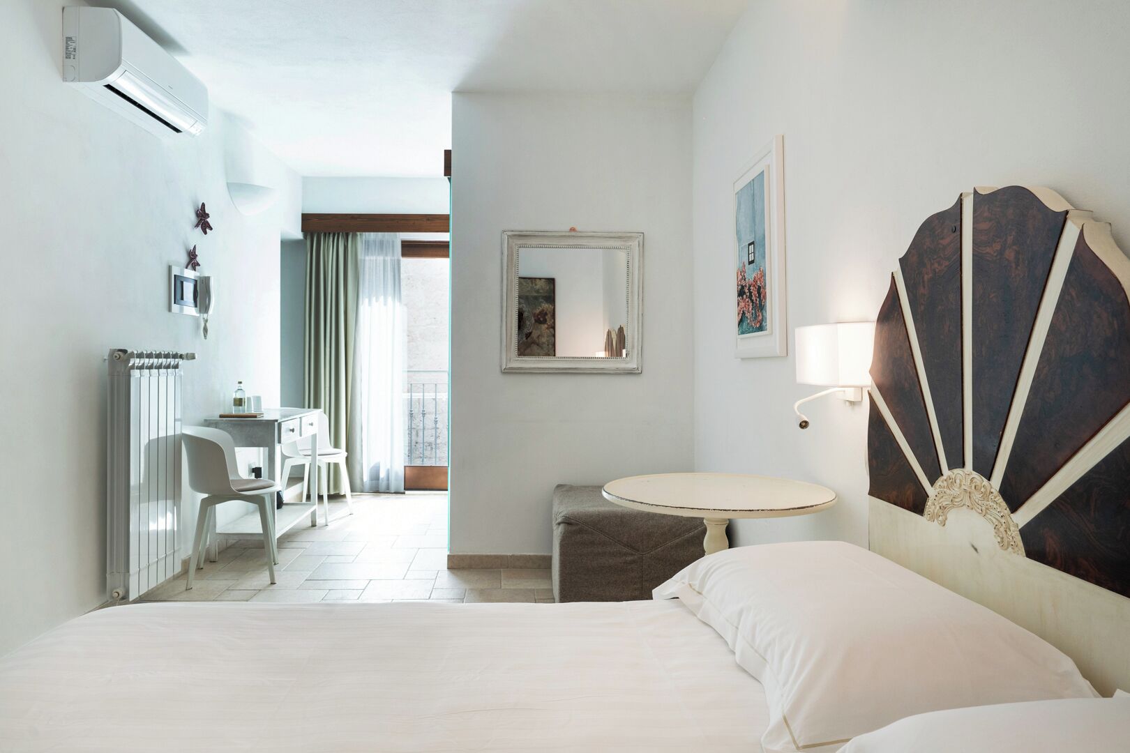 A hotel room with a bed, a desk, a chair, a small table, and a large decorative mirror.
