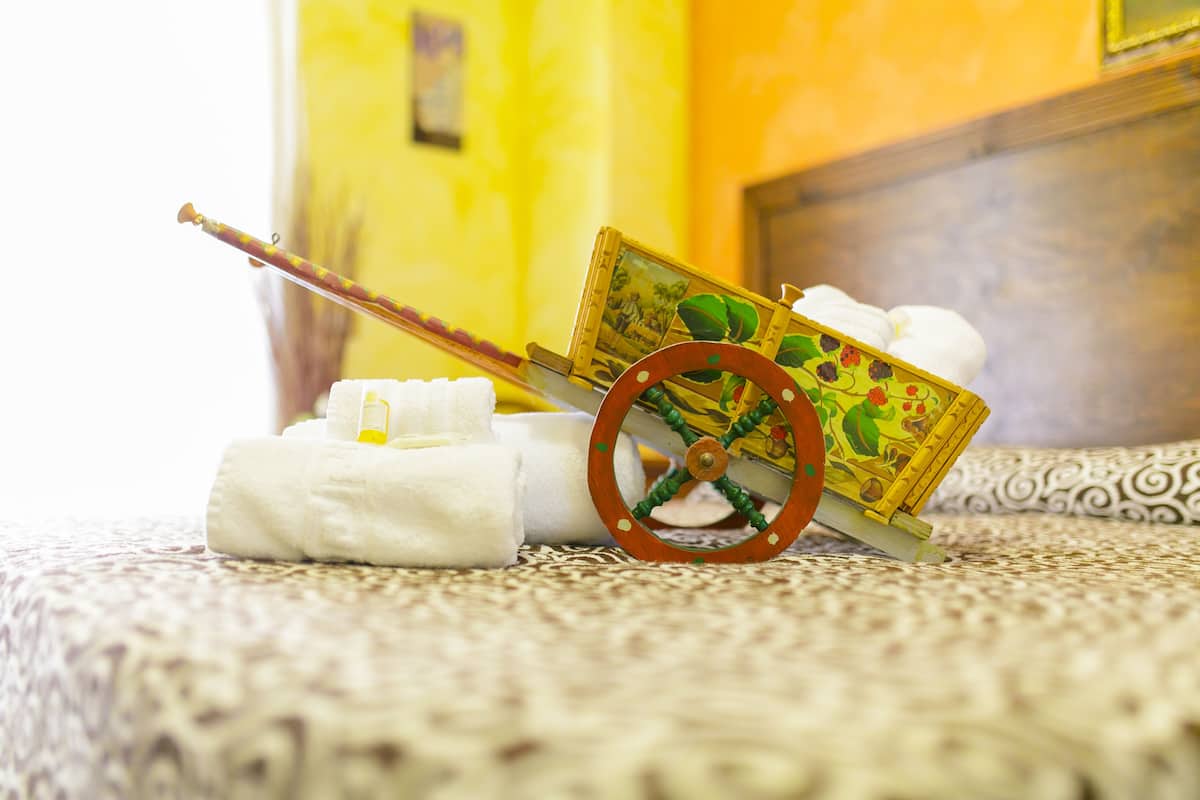 A bed with a patterned bedspread, a small wooden cart with a picture, and a white towel.
