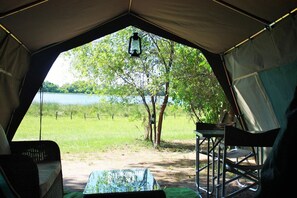 A tent with a view of a lake and trees, a table, and chairs inside. - Hippo Island Okavango Delta (Maun)