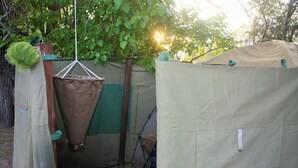 A garden with a hanging laundry basket, a green tarp, and a white tent-like structure. - Hippo Island Okavango Delta (Maun)