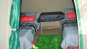 A small, enclosed space with two beds, each with patterned bedding and red pillows. A small table with a grid-like surface is placed between the beds. - Hippo Island Okavango Delta (Maun)