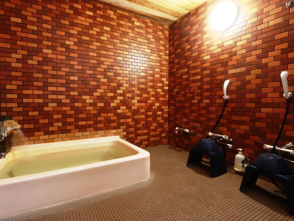 A bathroom with a brick wall, a bathtub, and a shower area with hoses and a soap dispenser.