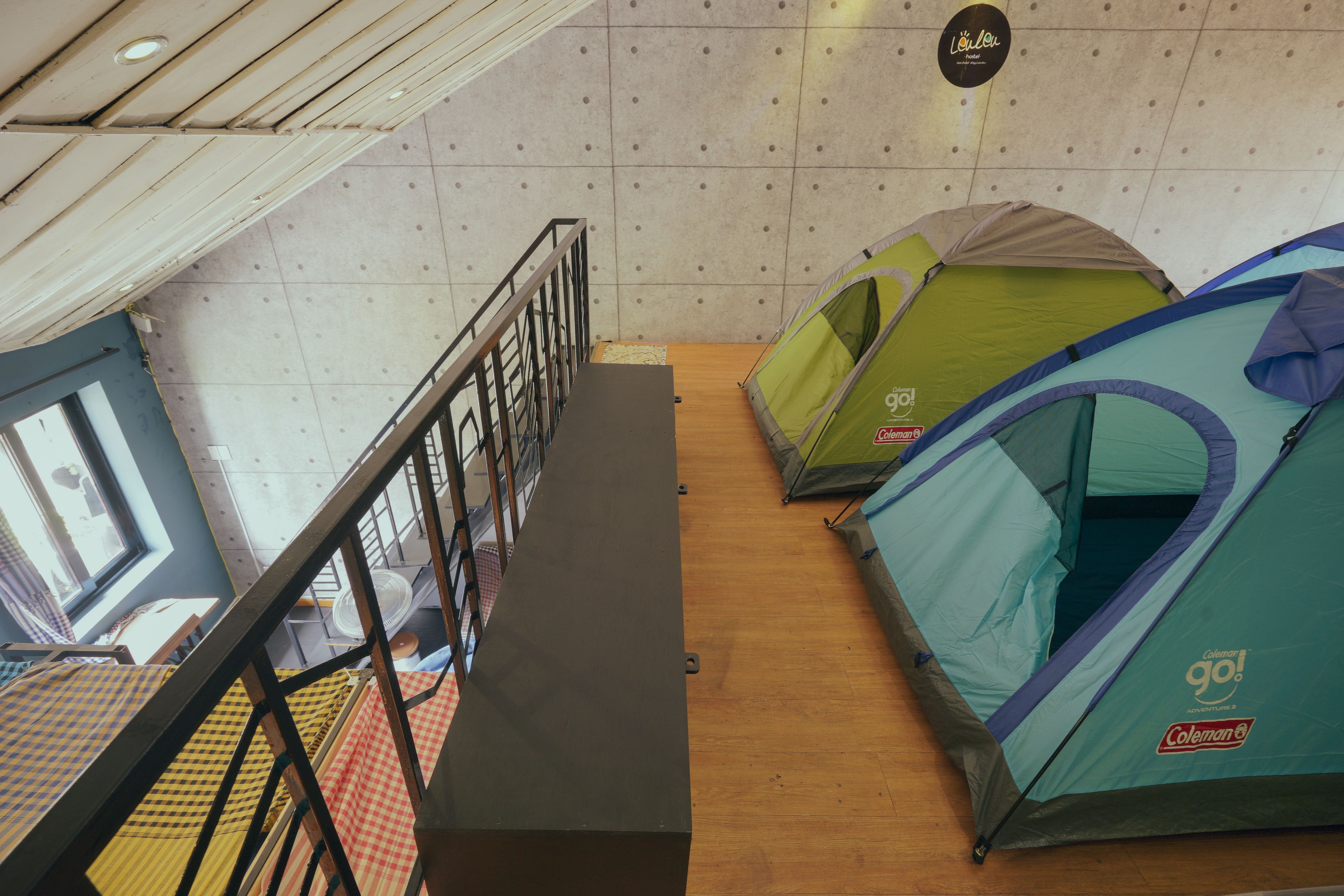 A room with multiple tents, a wooden floor, a metal railing, and a window with a view.