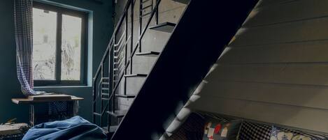 A loft-style room with a wooden floor, a large bean bag chair, a wooden bench, and a staircase.